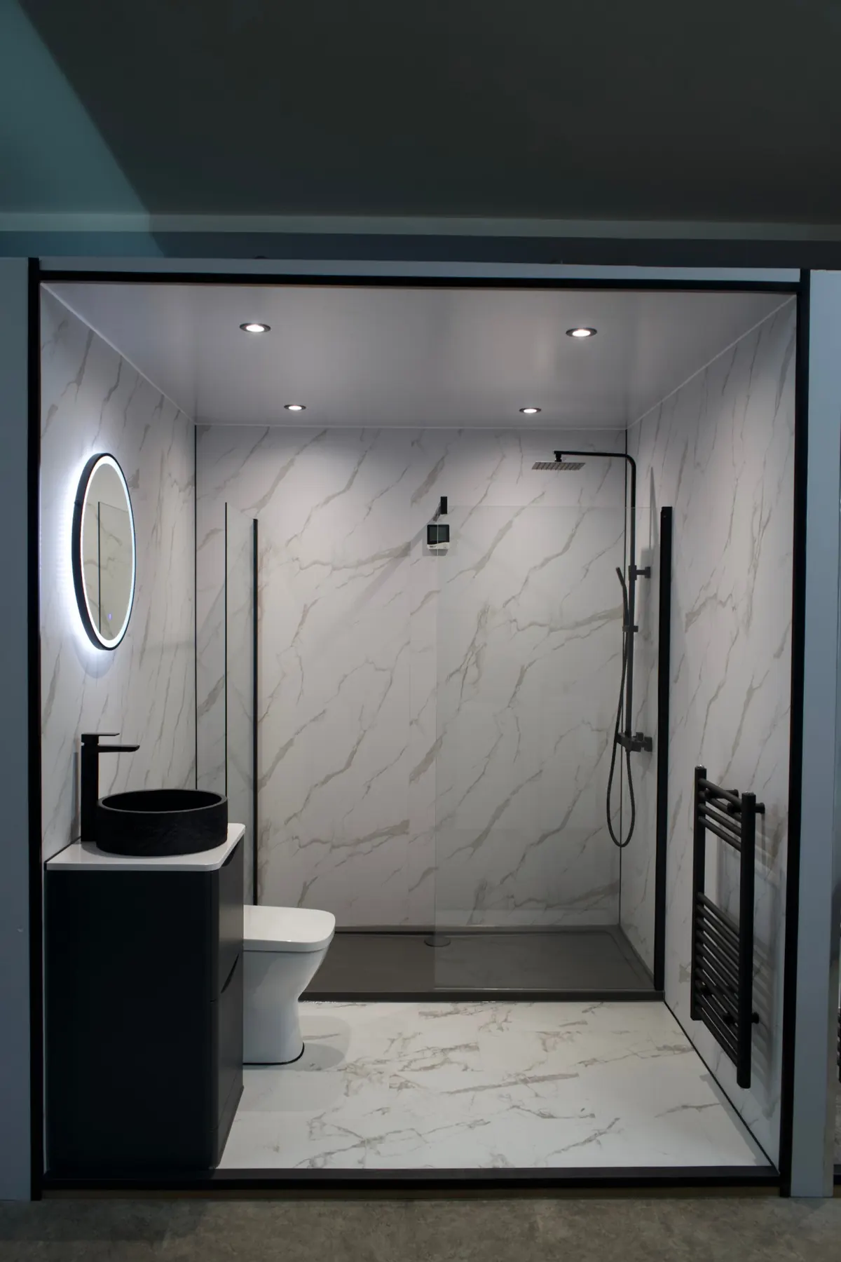 Walk-in shower with marble-effect wall panels and matt black fittings in our showroom